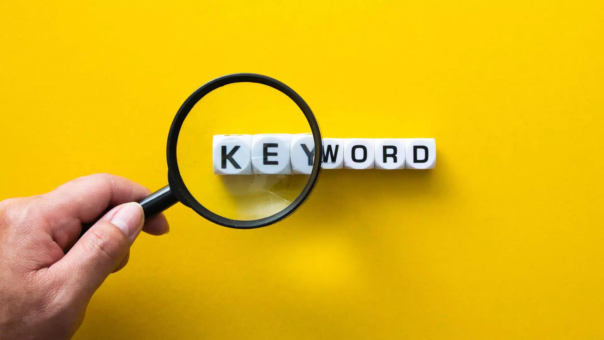 Mão segurando uma lupa sobre a palavra long tail keyward em fundo amarelo